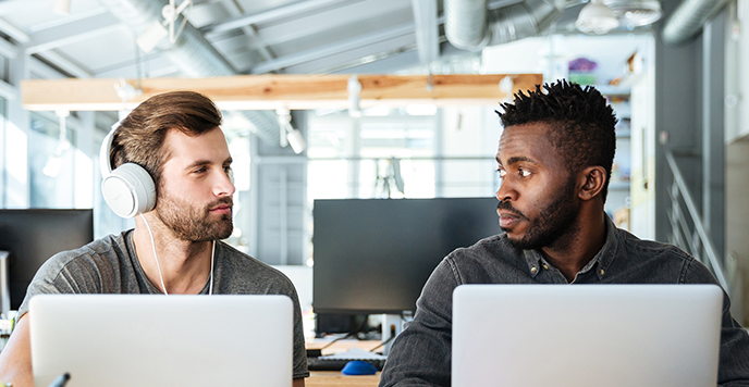 2 men at laptops looking at each other